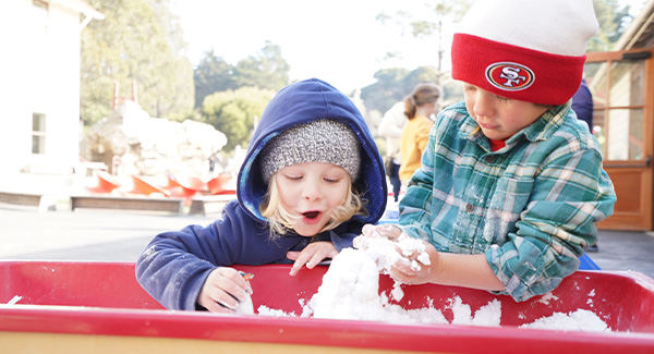 Two young children play with fake snow they made. The child on the left gasps with delight.