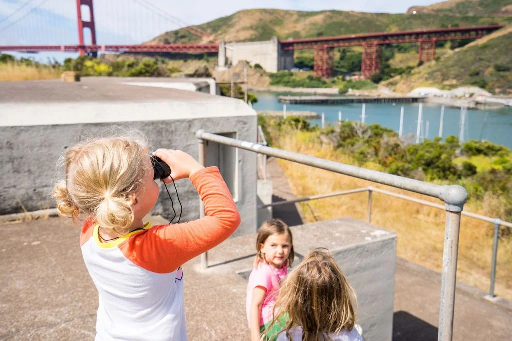 A young girl using binoculars to explore the Bay Area next to her two friends
