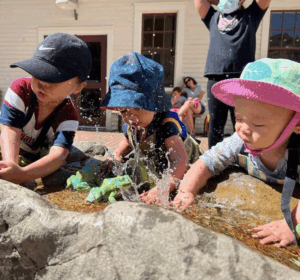 Three toddlers splash water in the Tot Spot Creek at the Bay Area Discovery Museum